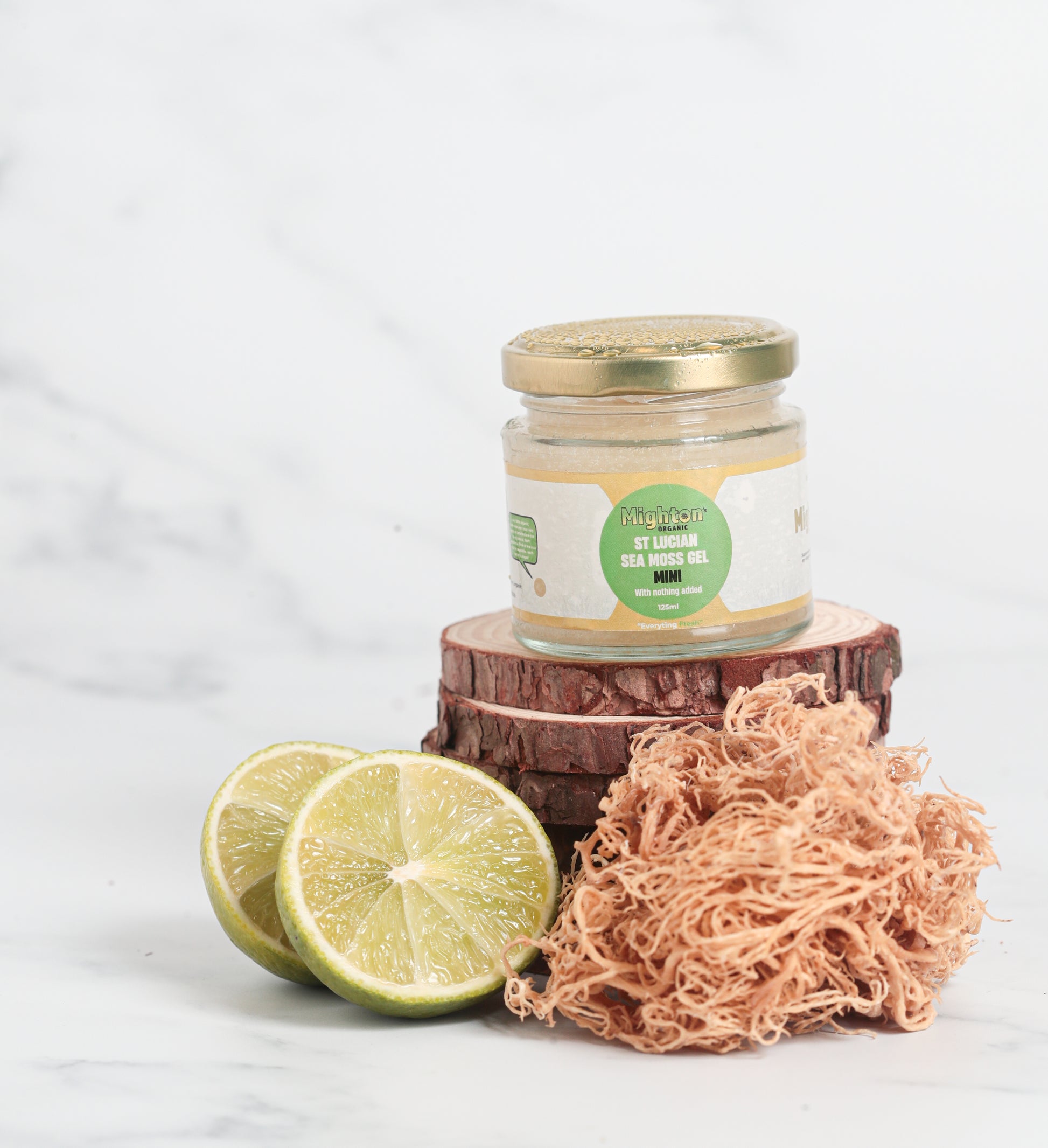 Small Jar of sea moss gel with a green label, sliced lime, and natural sponge on a white background