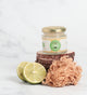Small Jar of sea moss gel with a green label, sliced lime, and natural sponge on a white background